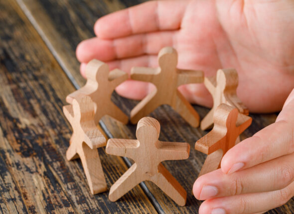 Business success concept on wooden background high angle view. hands protecting wooden figures of people.